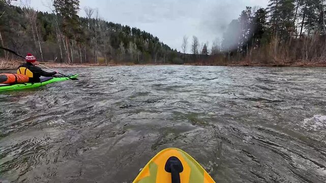 Caucasian teammate pursuing close through rapids, intense followshot as paddler maneuvers beside bow, spray and waves crash against hulls, high energy and teamwork in raw river setting.