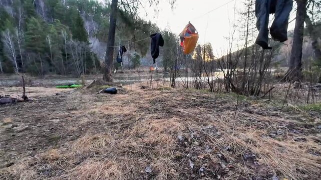 View from tent camping riverside, domestic campsite scene with clothesline drying jacket and socks above grassy bank at dusk, tent opening framing tranquil river valley and evening routine.