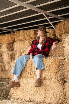 Woman relaxing on hay bale stack in barn, rural life
