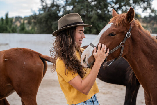 Young woman in hat petting horse at outdoor stable