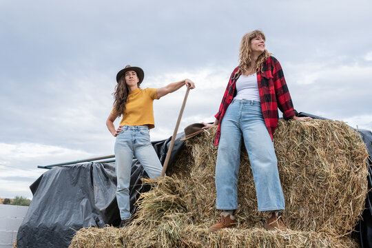 Two young woman standing on top of hay bale at rural farm