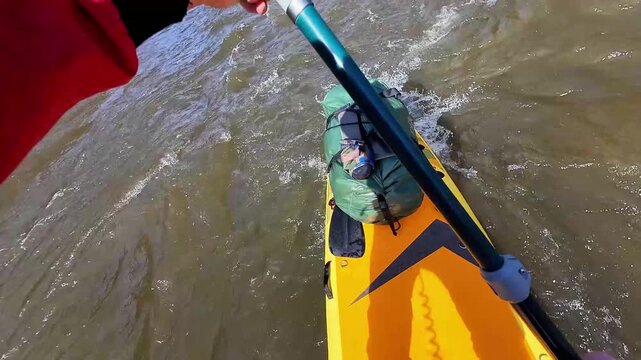 Paddler bracing in choppy river rapids, dynamic strokes to maintain balance, bow carving through waves, packed gear secured, intense focus and technical skill on turbulent water.