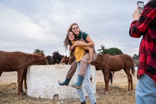 Young women posing by horses while friend takes photo