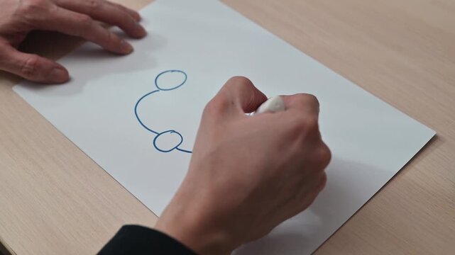 A person outlines circular shapes using a marker on a sheet of paper. This activity demonstrates creativity and design in a minimal workspace setting