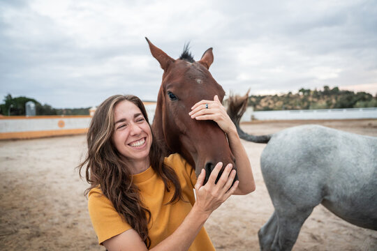 Woman hugging horse in outdoor paddock under cloudy sky