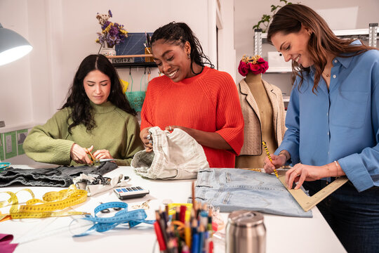 Multiethnic women cutting fabric and upcycling jeans
