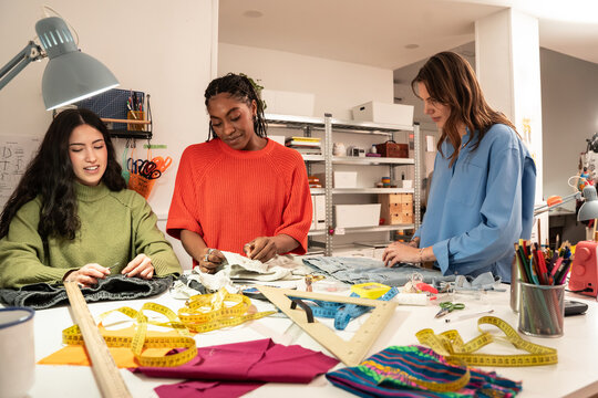 Multiethnic women sewing garments together in bright atelier