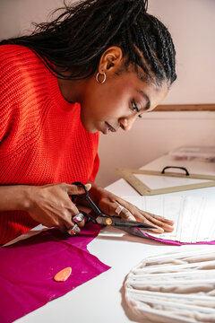 Black colombian woman cutting fabric for garment pattern in atelier