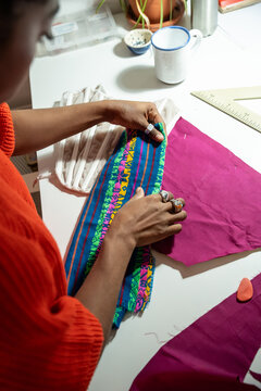 Woman sewing colorful trim on garment at fashion atelier