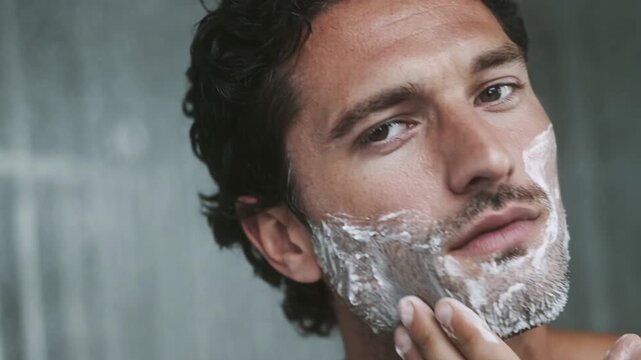 Good looking man spreading shaving foam on his cheeks and beard before shaving