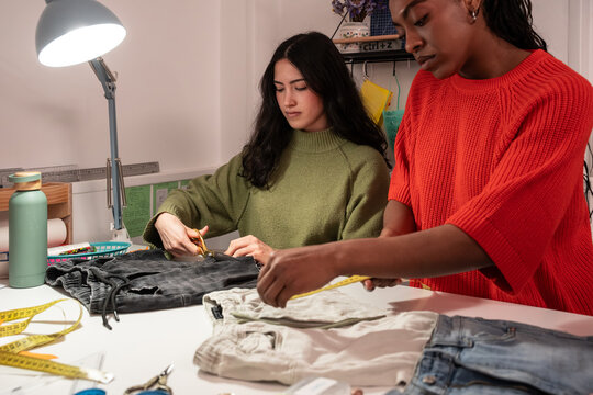 Multiethnic women sewing and measuring garments in atelier