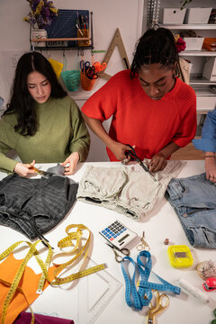 Multiethnic women cutting fabric and upcycling jeans