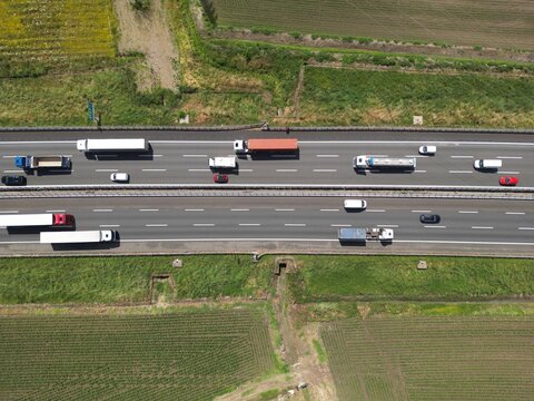 Highway Traffic Flow: An aerial view captures the bustling activity on a multi-lane highway, with various trucks and cars navigating the asphalt under a clear sky.