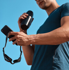 Fototapeta premium Hands, athlete and man with cellphone outdoor for texting, networking or contact at practice. Water bottle, fitness and male swimmer with phone for social media on mobile app at competition training.