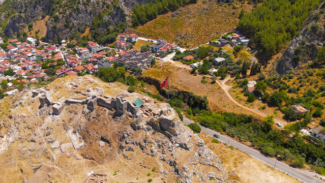 Fethiye, Turkey. Large Turkish flag flying on flagpole atop the historic Fethiye Castle hill with ancient Lycian rock cut tombs in the surrounding cliffs, drone footage.. Aerial View