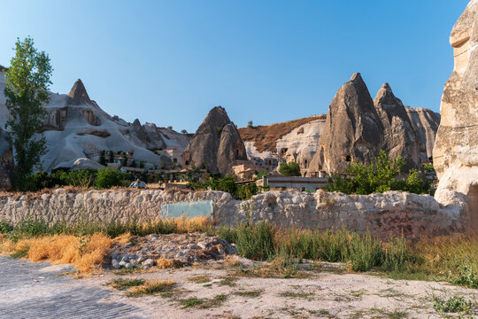 Goreme, Nevsehir, Turkey. Fairy chimney rock formations and ancient cave dwellings carved into volcanic tuff cliffs, morning sunlight illuminating the textured stone landscape under a clear blue sky