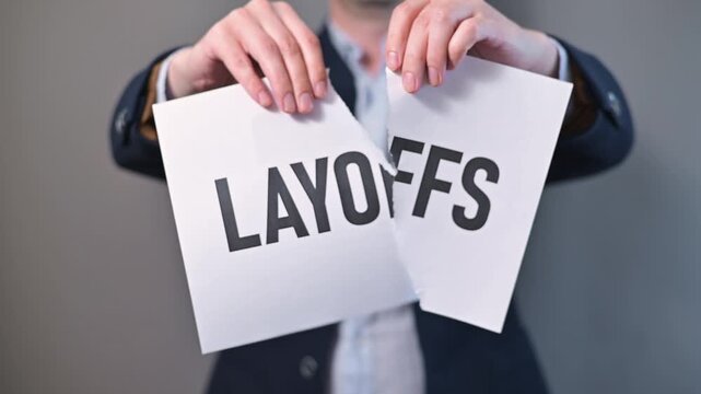 An individual takes action against layoff notices in a corporate space, tearing papers while standing. This is a common response to job loss in various industries during difficult times