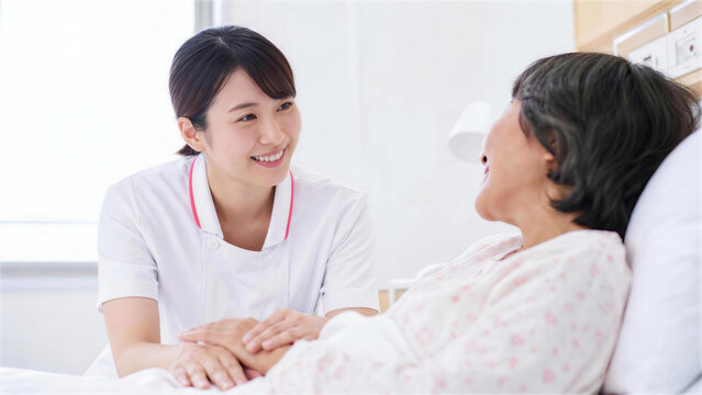 ベッドに寝ているシニア患者の手を握り笑顔で会話する看護師