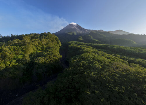 Aerial view of Mount Merapi volcano with smoke rising from the crater above the lush green forests of Bunker Kaliadem in Kecamatan Pakem, Daerah Istimewa Yogya, Indonesia.