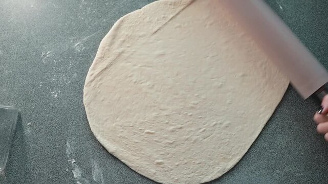 A person rolls out dough using a rolling pin on a countertop in a kitchen setting. The action focuses on preparing dough, highlighting the process of baking