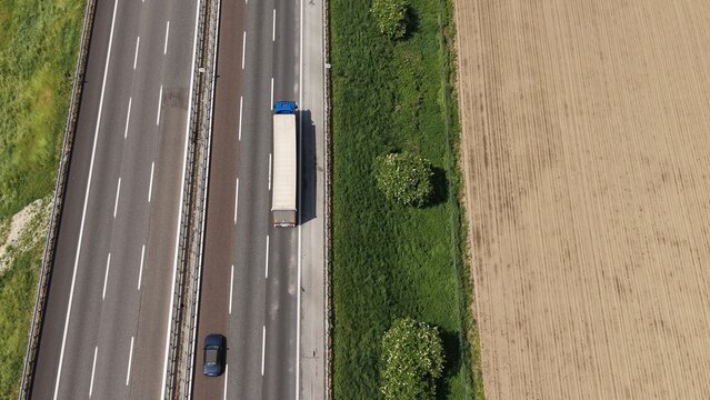 Highway Truck and Car Aerial View: An aerial perspective captures a truck and car traveling on a highway adjacent to agricultural fields under a clear sky.