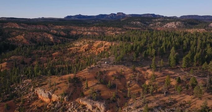 Pine forest and orange sandstone ridges spread across Dixie National Forest Utah plateau terrain, drone panoramic orbit