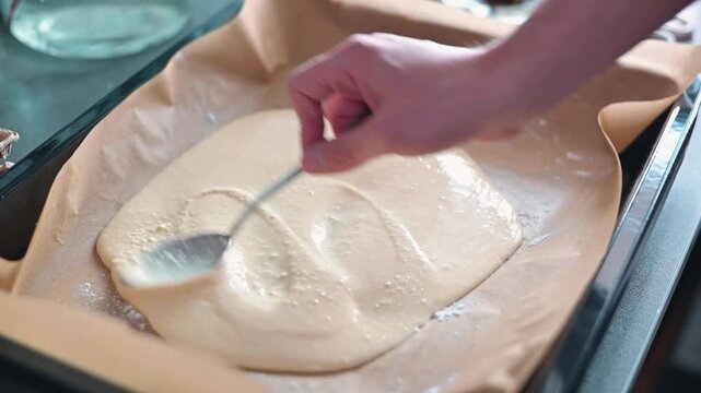 A person is stirring a mixture on parchment paper laid in an oven pan while preparing a dessert in a kitchen.