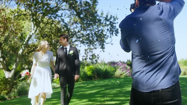 Bride and groom starting walking on lawn to camera, confetti falling, pro shooting wedding photos