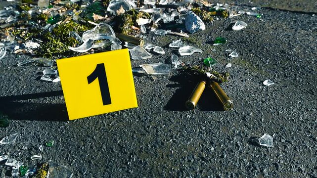 Evidence marker number one identifying bullet casings and shattered glass on the asphalt at a crime scene, symbolizing a violent encounter such as a shooting, murder, or terrorist attack
