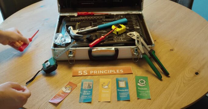 Hand holding &ldquo;Sort&rdquo; 5S card while organizing tools, representing removal of unnecessary items and workplace efficiency.