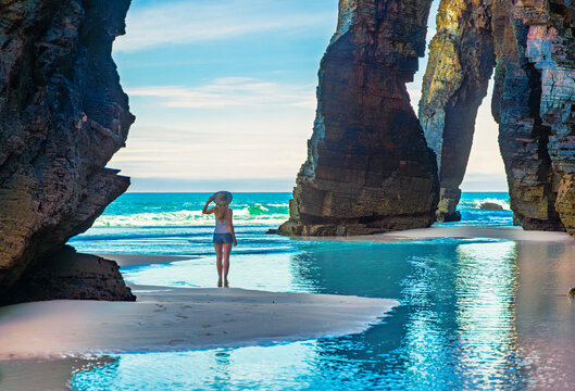 Woman tourist walking between giant rock arches at Playa de las Catedrales in Ribadeo, Galicia, Spain