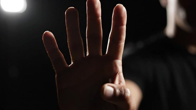 Hand Silhouetted Against a Black Background Displaying Four Fingers Signifying Countdown or Agreement
