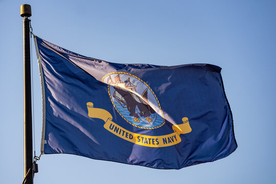 Navy flag waves beside blue sky. Outdoor navy banner supports patriotic concept. Navy heritage reflects military service tradition. US Navy symbol represents american maritime authority.