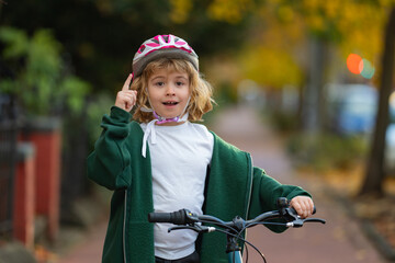 Obraz premium Child rides bike on autumn. Kid portrait with bike helmet with idea. Safe kid cycling on street. Happy child learning to bike ride. Fun outdoor activity for children. Child with bicycle in autumn fall