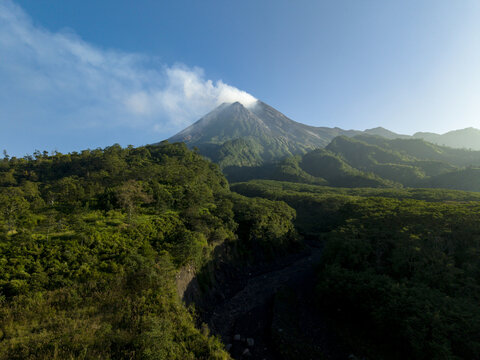 Aerial view of Mount Merapi with smoke rising from the crater above lush green tropical forests and a deep valley Kecamatan Pakem, Daerah Istimewa Yogya, Indonesia.