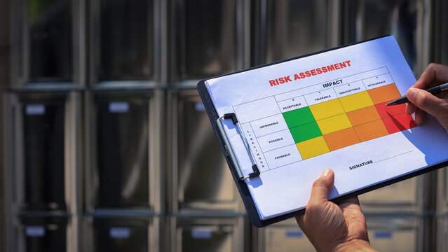 Focused worker conducting hazard analysis holding clipboard with risk matrix paper during logistics operations near metal storage shelf