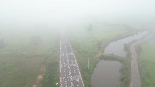 Aerial view of misty paddy field and country road surrounding a rural village at dawn. These areas serve as one of the country's most important rice-producing regions in Thailand.