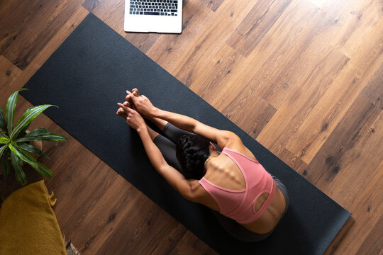 Woman practicing yoga at home, stretching with online class
