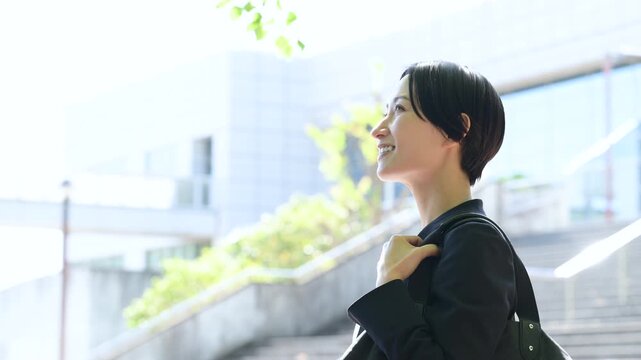 ビル背景で笑顔で歩むビジネス営業女性の横顔、転職や採用などの明るいミドル層の前向きと成長イメージの動画スローモーション