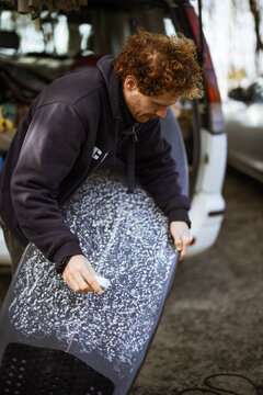 Surfer waxing surfboard by van preparing for outdoor lifestyle