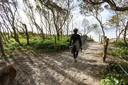 Surfer walking with surfboard on sandy path towards the ocean