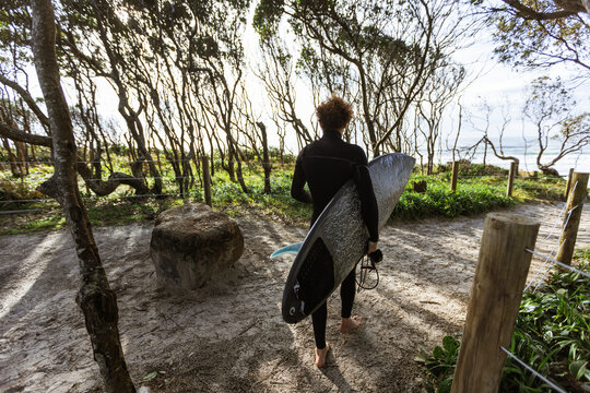 Surfer walking with surfboard on sandy path to beach