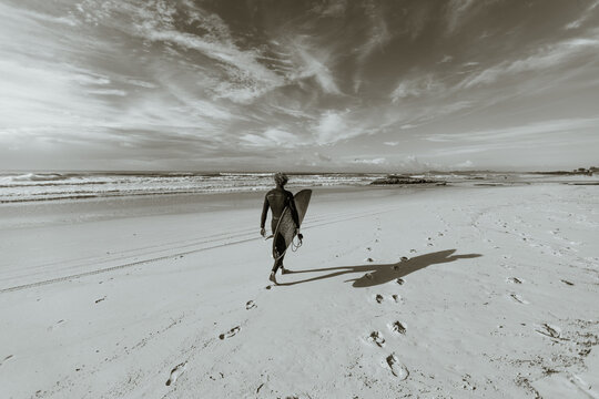 Surfer walking to ocean with surfboard at beach