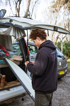 Young man assembling surfboard fins while standing by his van