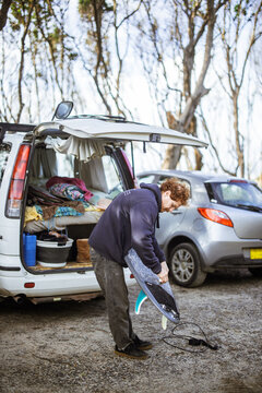 Surfer standing next to a camper van, attaching leash to a surfboard
