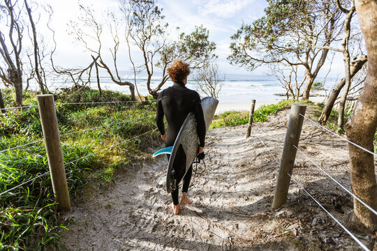 Surfer walking with surfboard on sandy path towards the ocean
