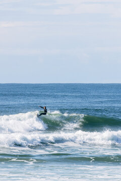 Surfer in wetsuit riding a blue ocean wave on a sunny day
