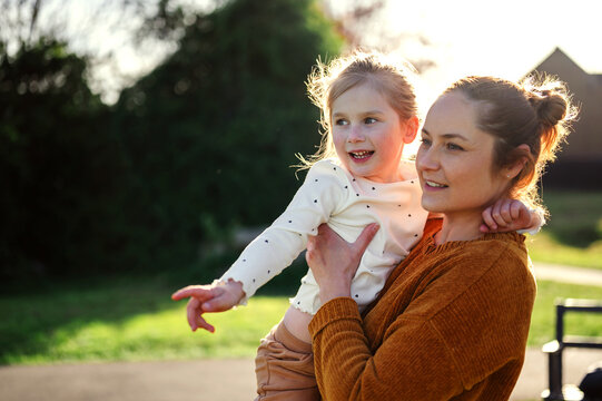 Mother holding daughter in sunlight, sunset light, copy space
