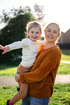 Mother holding daughter in sunlight, summer time