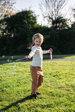 Little girl playing with bubbles in sunlight outdoors